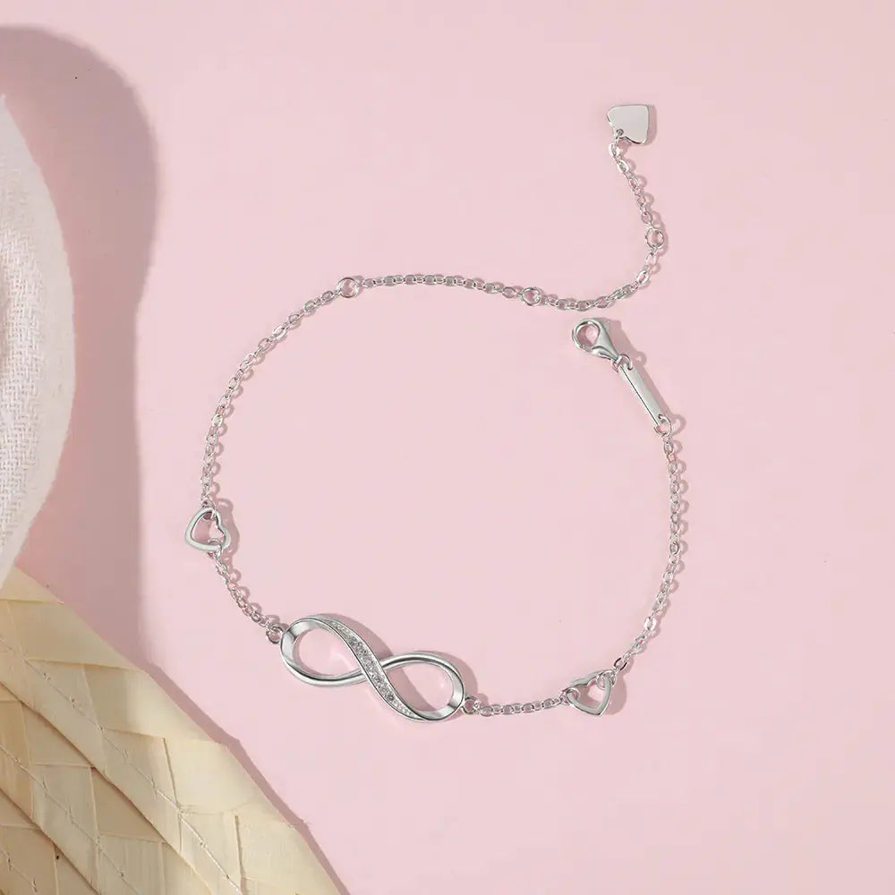 a white hat and a silver bracelet on a pink surface