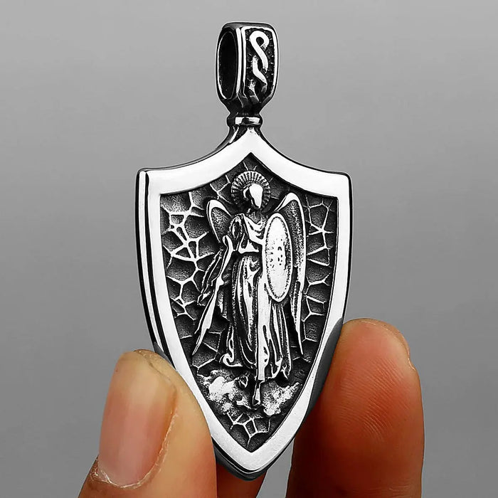 a hand holding a silver pendant with an angel on it