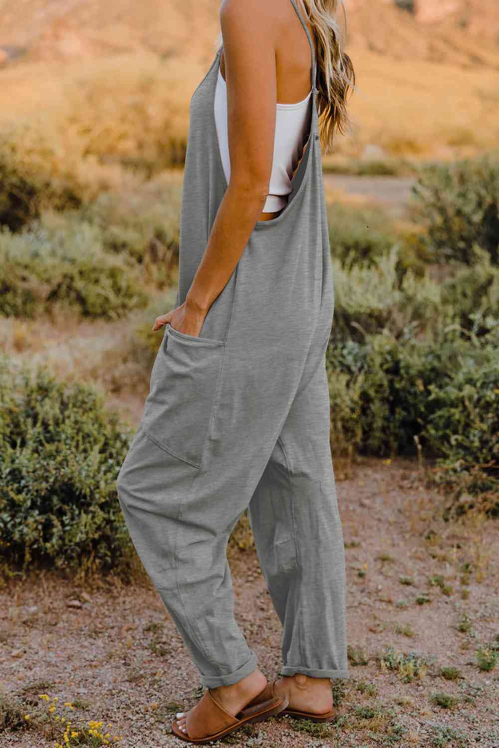 a woman standing in a field wearing a grey jumpsuit